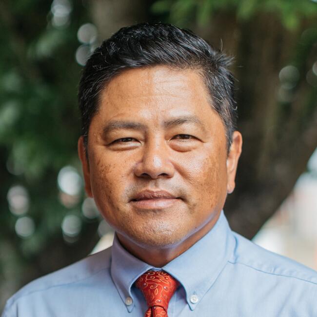 Juancho Ramirez smiles at camera outside in blue collared shirt and orange tie