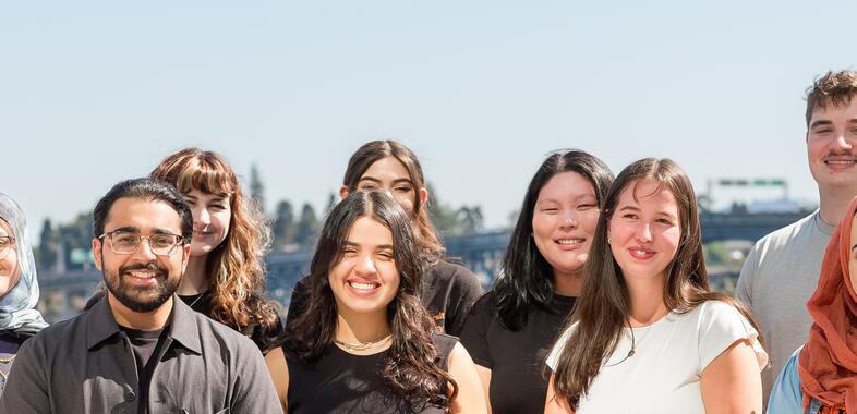 Group of students smile at camera out in the sunshine with portland in the background