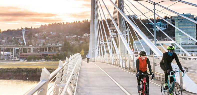 Two people bike across the Tillikum bridge in Portland, OR