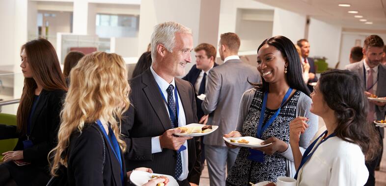 A group of older professionals speak in a circle while eating