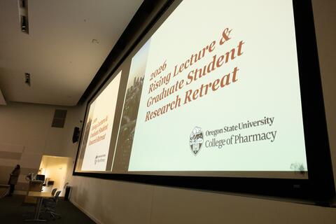 A presentation slide in front of a lecture hall says "2026 Rising Lecture & Graduate Student Research Retreat"